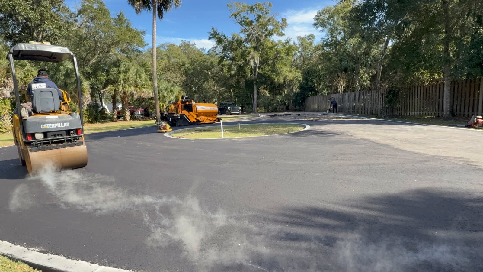 Roller compacting fresh asphalt on a newly paved cul-de-sac with the paver working in the background
