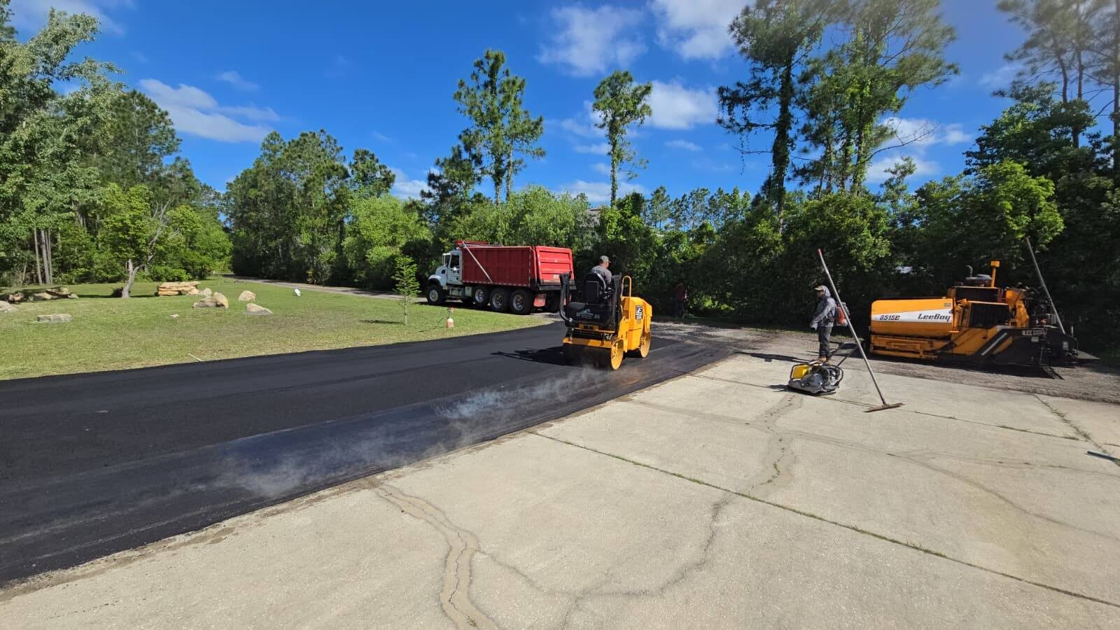 Paver and roller laying a new asphalt lane alongside an existing cracked concrete surface