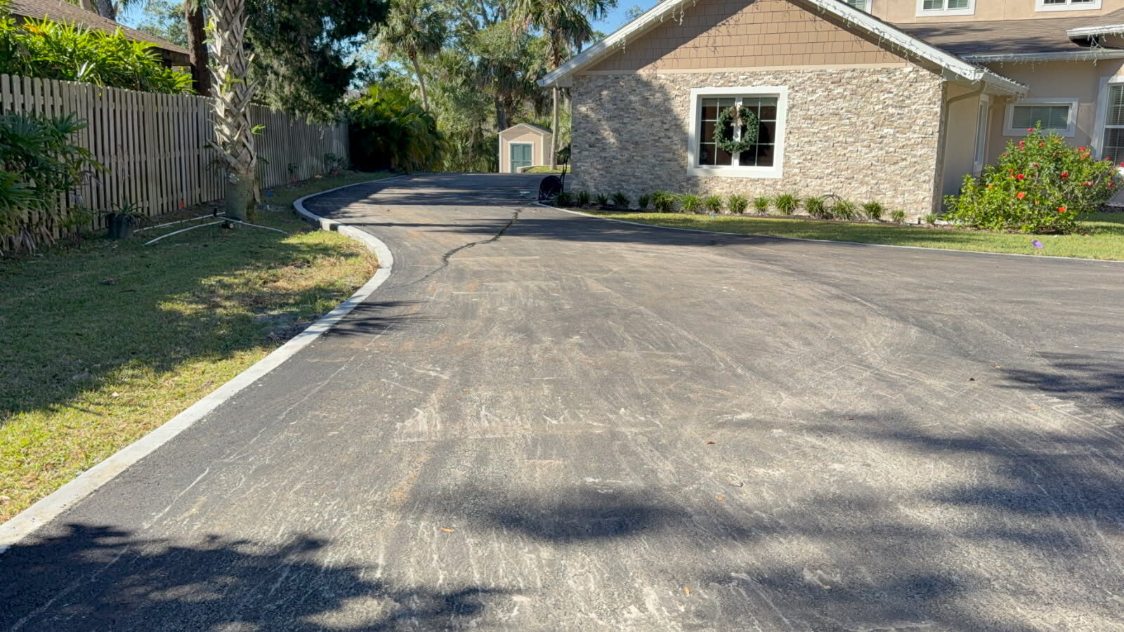 Finished asphalt driveway curving up to a Florida home with a concrete curb edge
