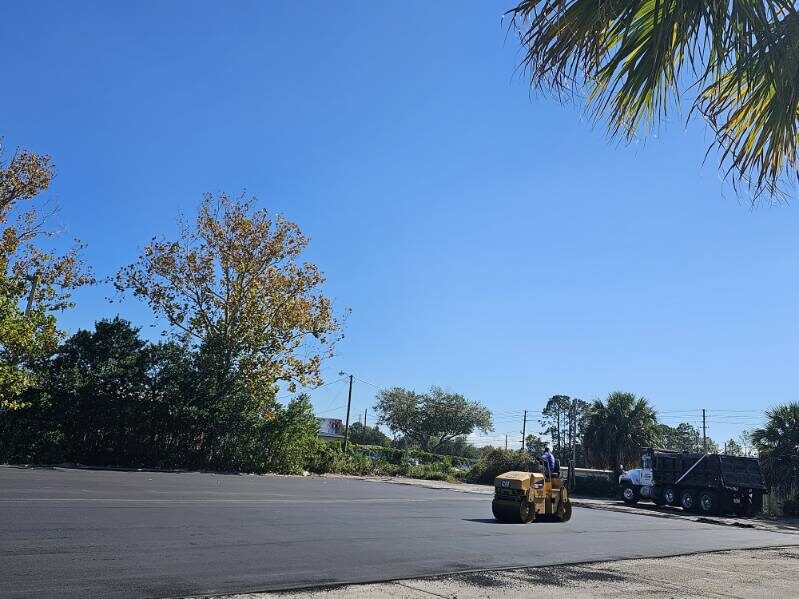 Roller compacting a large new commercial asphalt lot with a dump truck standing by in Central Florida
