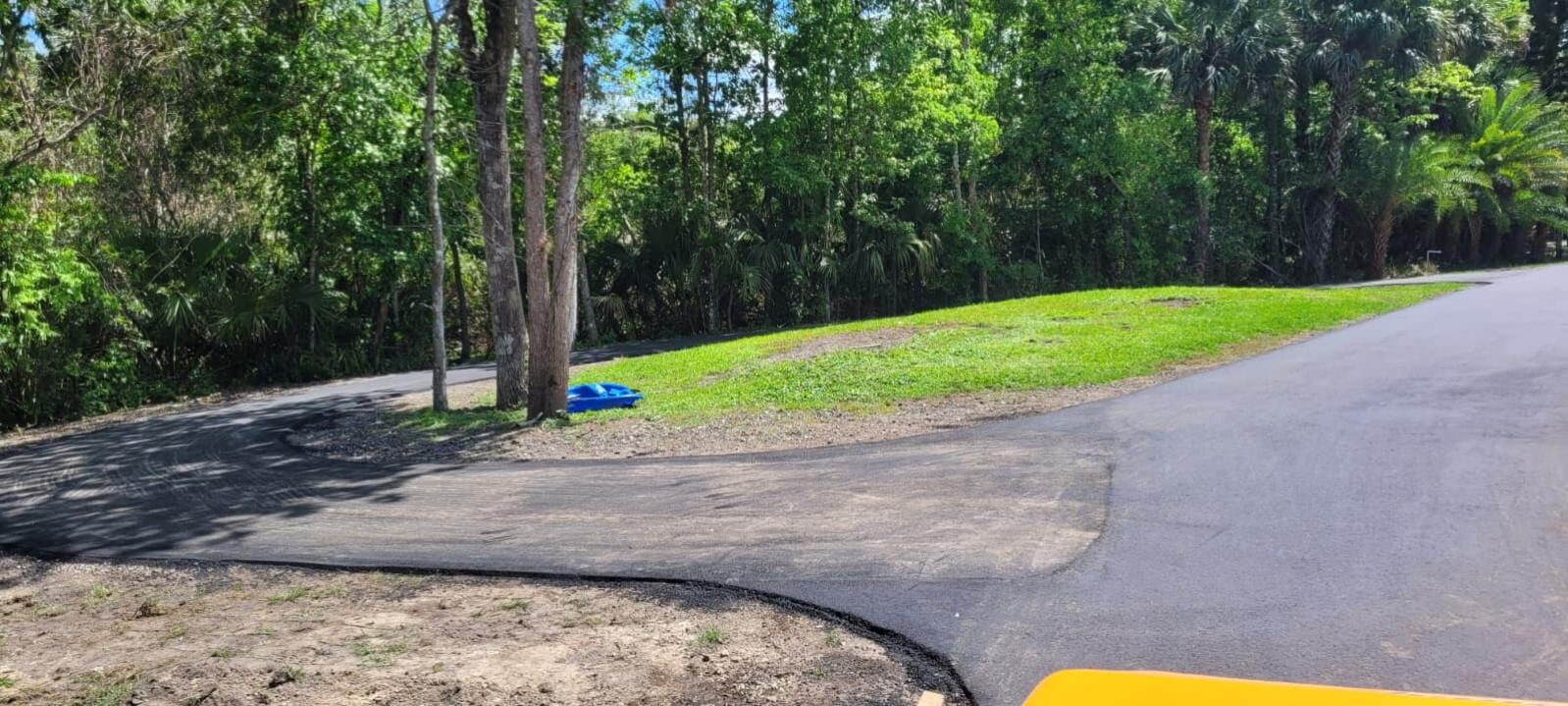 Deep black asphalt surface tying into an existing drive through a wooded Florida property