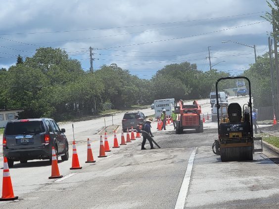 Traffic cones channeling vehicles past an M&S Asphalt Paving crew and roller during a commercial roadway job
